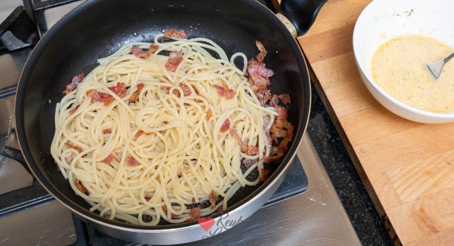 Roer de spaghetti door het spek
